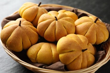 Wicker basket with tasty pumpkin shaped buns on dark table, closeup