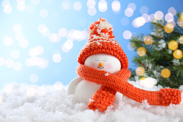 Cute decorative snowman on artificial snow against blurred lights. Space for text