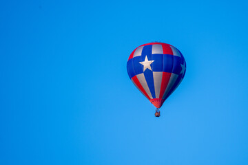 Hot air balloon in the distance in red blue and silver with 5 pointed star against a deep blue sky.