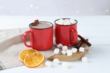 Yummy cocoa with marshmallows, dried orange slices and spices on white wooden table