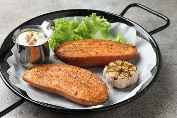 Tasty cooked sweet potato served in baking dish on grey textured table, closeup