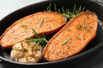 Halves of tasty cooked sweet potato with rosemary and garlic in baking dish on grey table, closeup