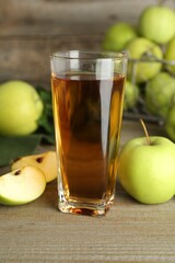 Glass of juice and apples on wooden table