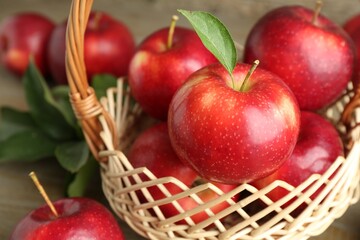 Fresh ripe red apples in wicker basket on wooden table, closeup