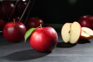Fresh ripe red apple with green leaf on black wooden table, closeup