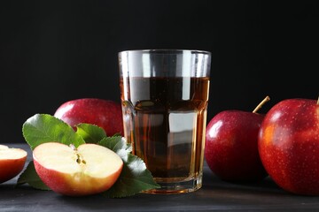 Tasty fresh apple juice in glass and fruits on black wooden table, closeup