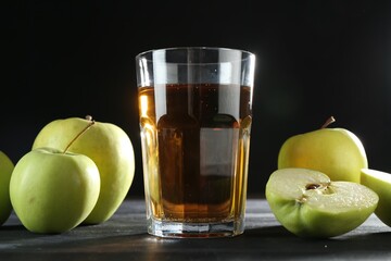 Tasty fresh apple juice in glass and fruits on black wooden table, closeup