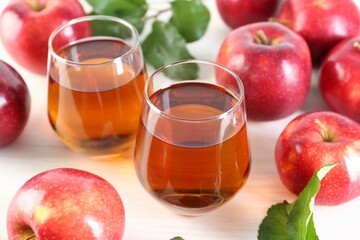 Fresh apple juice in glasses, fruits and green leaves on white table, closeup