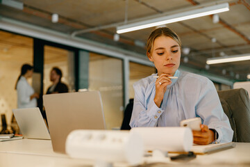 A young woman is actively engaging with her smartphone while situated in a contemporary office environment