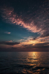 Obraz premium A stunning sunset over the sea, with a starry night sky and faint galaxy emerging, reflected in the clear ocean water, creating a peaceful and captivating natural landscape