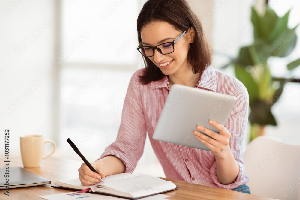 Poster e-learning. young woman in glasses holding tablet computer and writing with left hand in notebook, s