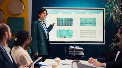 Marketing specialist evaluating market trends by studying infographics with her coworkers in a...