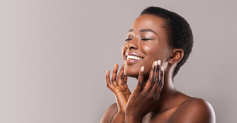 Face lifting concept. Happy black woman with closed eyes touching soft smooth skin on her cheeks...