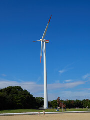 海の海岸の公園で散歩する人々の姿と高い風力発電機の様子