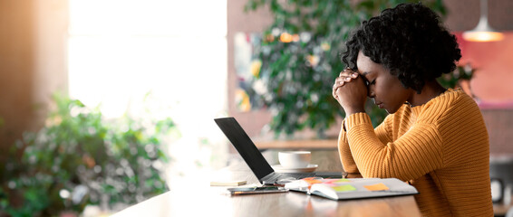 Exhausted african american girl sitting in cafe, looking for job online, using laptop, empty space