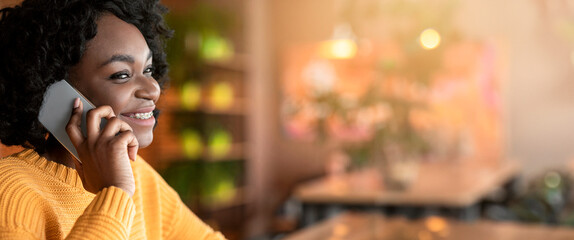 Side view of young african woman talking by modern smartphone, cafe interior, close up