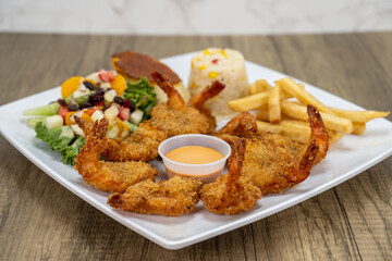 Breaded shrimp empanizados arranged around dipping sauce served with french fries and salad for a delicious seafood meal