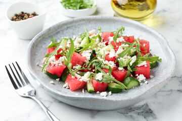 Delicious watermelon salad with feta cheese, cucumber and arugula served on white marble table, closeup
