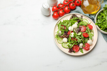 Tasty salad with arugula, lettuce, mozzarella cheese and vegetables on white table, flat lay. Space for text