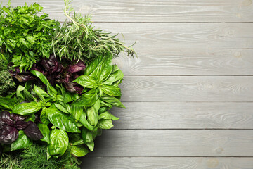 Different fresh herbs in basket on light grey wooden table, top view. Space for text