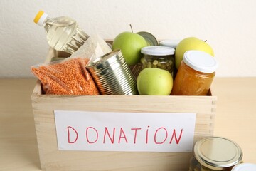 Different donation food products in crate on wooden table, closeup