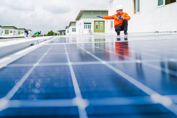 A worker in an orange safety jacket inspects solar panels on a rooftop, using a laptop to ensure...