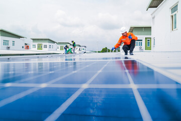 A worker in an orange safety jacket inspects solar panels on a rooftop, using a laptop to ensure...