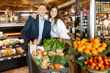 Portrait of a positive happy young couple with products in a cart, who came to the supermarket for...