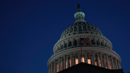 Obraz premium Off center to right closeup of US Capitol dome with flags waving in Washington DC at night with lights on the architecture. Copy space on left.
