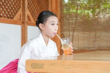 A 9-year-old Korean girl wearing a hanbok is drinking a beverage inside a traditional building in the historic town of Gyedong-gil, Jongno District, Seoul, Korea.