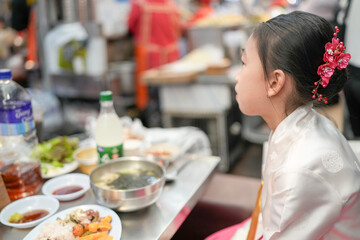 A 9-year-old Korean girl wearing a hanbok is eating a meal at a local market in Changgyeonggung-ro, Jongno District, Seoul, Korea.