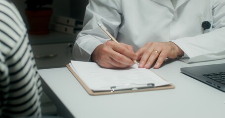 A male doctor writes in a notebook, making an appointment for treatment to a patient. Close-up of his hands, an unrecognizable person