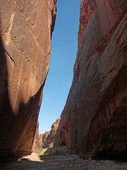Hiking inside Buckskin Gulch, walking by footpath between narrow red rock sandstone canyon walls...