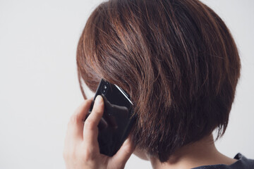 スマホで通話をするアジア人の中年女性の後ろ姿