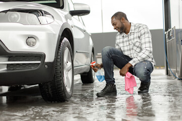 Middle aged black man with a sprayer bottle for polishing car in the car wash