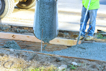 Concrete mixer truck is pouring fresh concrete onto reinforced bars for new sidewalk