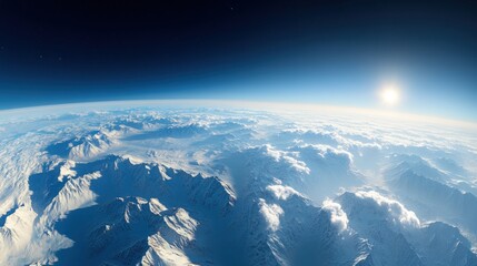 Naklejka premium A panoramic view of snow-capped mountains extending to the horizon, with the sun shining above the clouds.