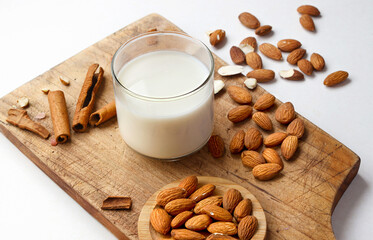 A glass of vegan almond milk on a wooden table, with whole almonds around. Non dairy milk, almond...