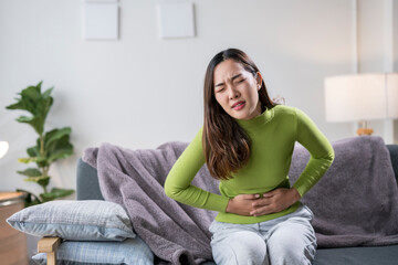Young woman suffering from strong stomach ache while sitting on sofa at home