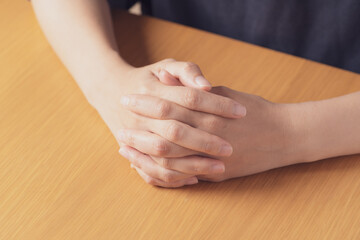 机の上で両手を組むアジア人の中年女性の手元