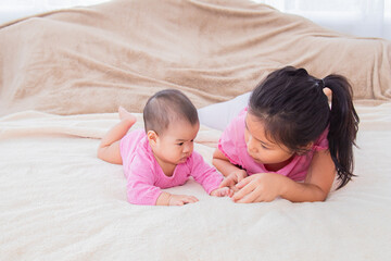 Asian happy cute big sister playing with adorable newborn baby girl in morning after waking up....