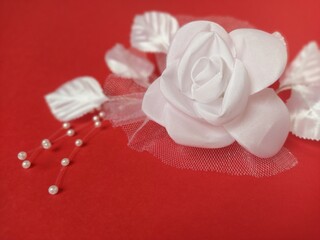 A stunning white rose stands out beautifully against a rich red background, complemented by soft leaves and small pearl accents, ideal for a wedding setting