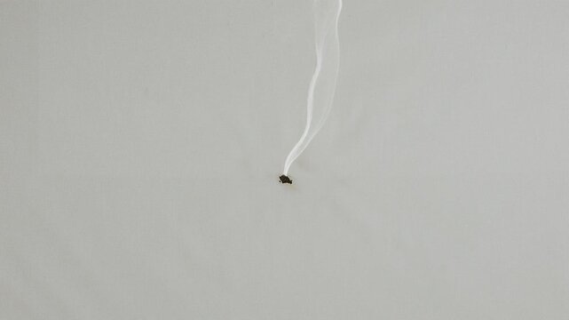 Overhead shot of small burn hole emitting smoke in light fabric