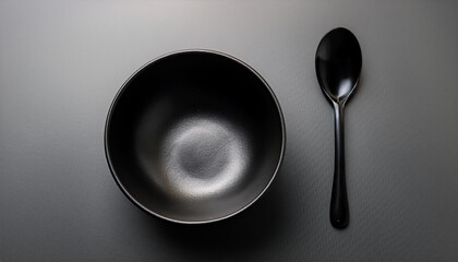 An empty black bowl and a table spoon in dark tone light studio ; minimal concepts with empty space for texting or for menu layout