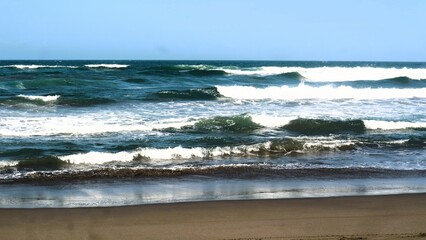 Waves crashing against the shore with a clear blue sky in the background at Parangtritis Beach, Yogyakarta.