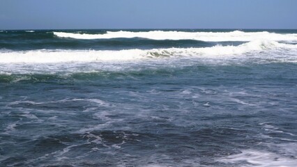 Waves crashing against the shore with a clear blue sky in the background at Parangtritis Beach, Yogyakarta.