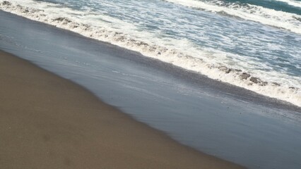 Waves crashing against the shore with a clear blue sky in the background at Parangtritis Beach, Yogyakarta.