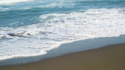 Waves crashing against the shore with a clear blue sky in the background at Parangtritis Beach, Yogyakarta.