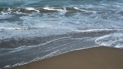 Waves crashing against the shore with a clear blue sky in the background at Parangtritis Beach, Yogyakarta.