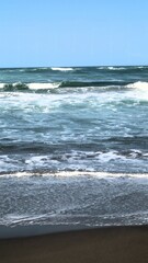 Waves crashing against the shore with a clear blue sky in the background at Parangtritis Beach, Yogyakarta.
